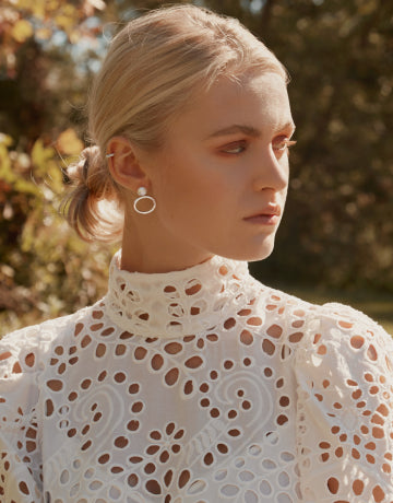 Woman wearing a white lace top with a blurred natural background