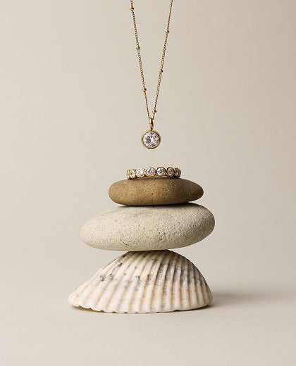 Necklace with a pendant on a stack of stones and a shell against a beige background
