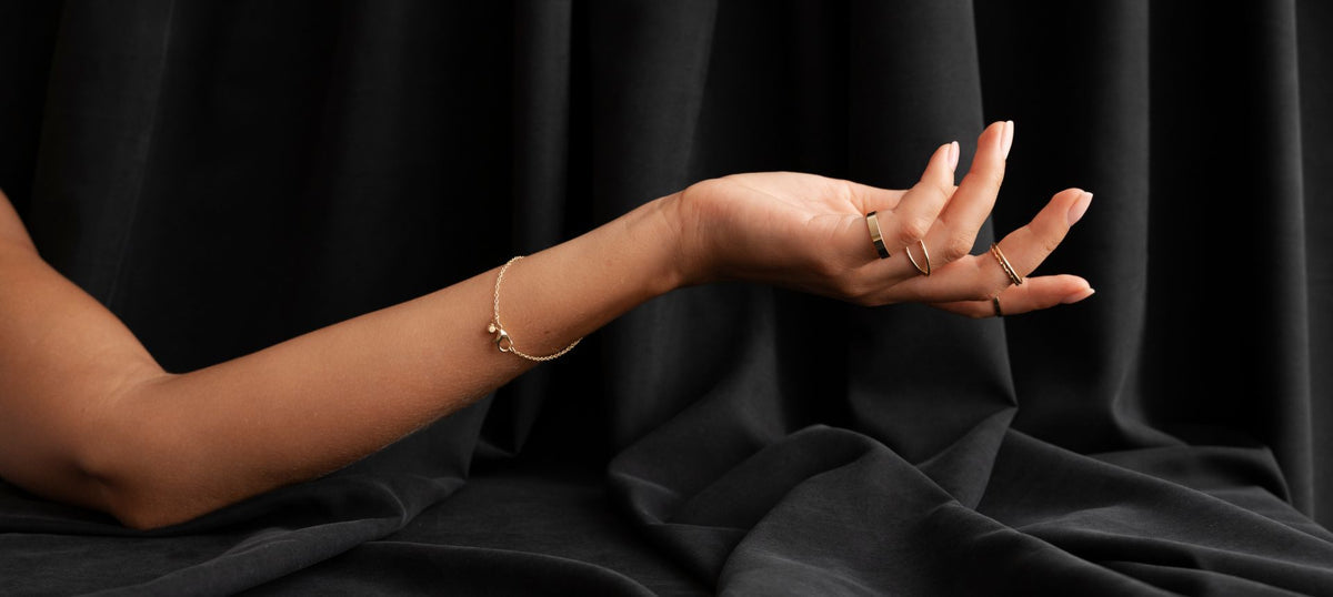 Hand with gold rings and bracelet against a black fabric background