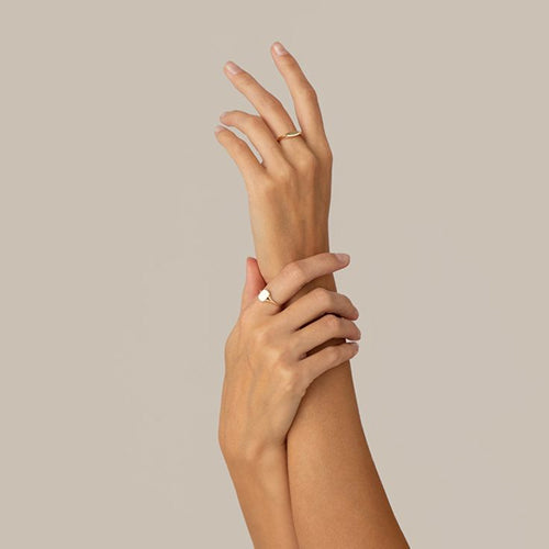 Two hands with gold rings on a beige background