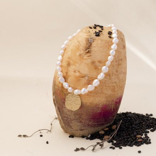 Pearl necklace with a gold tag on a wooden block with black seeds