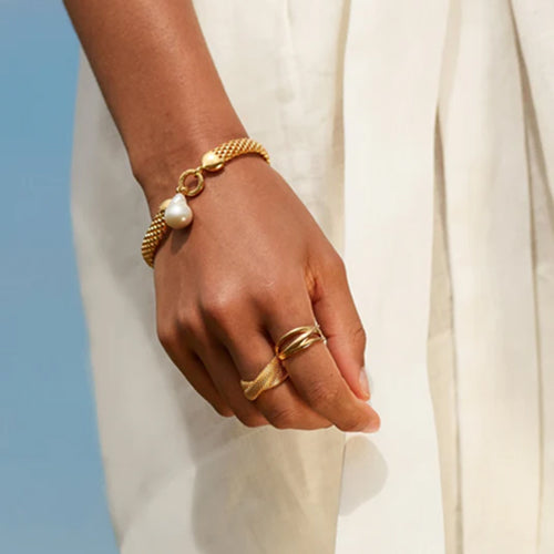 Hand wearing a gold bracelet and ring with a plain background