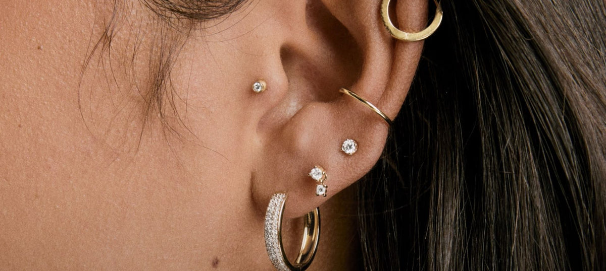 Close up of an ear with multiple gold and silver earrings